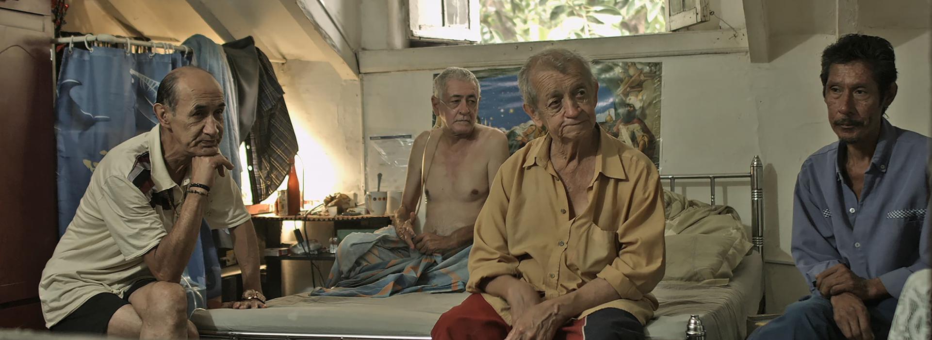 Cuatro hombres están sentados en una habitación. Uno de ellos está enfermo y lleva un respirador.