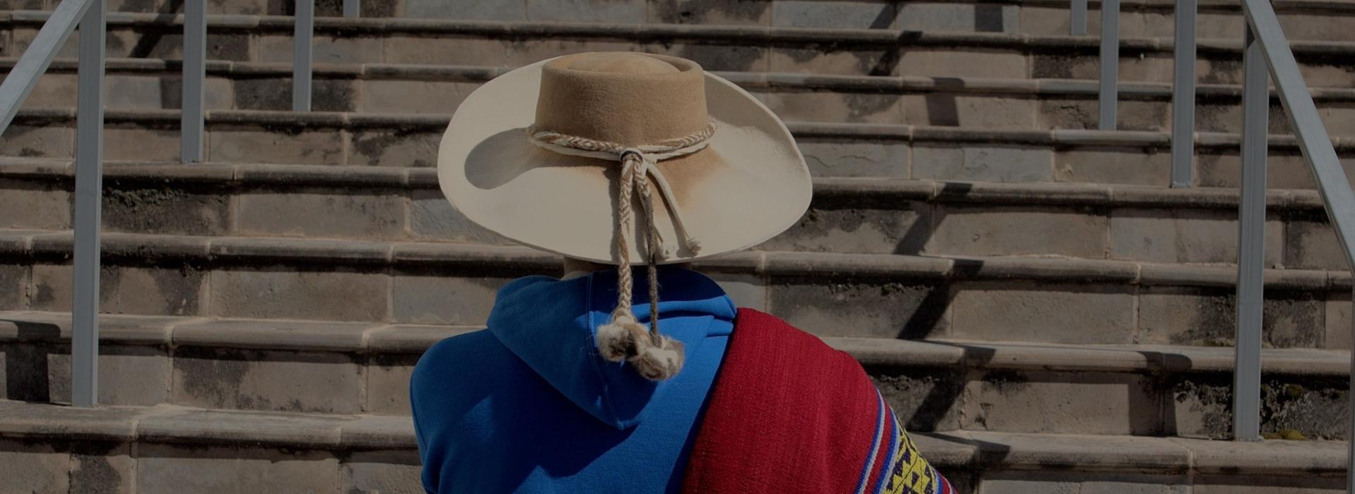 Una persona de espaldas con un sombrero delante de unas escaleras.