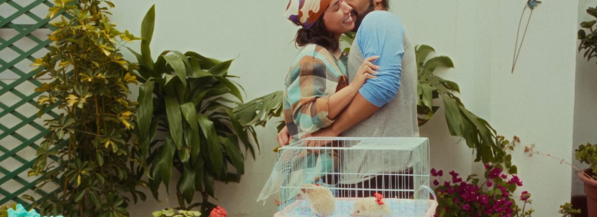 Una pareja se abraza delante de una jaula con dos erizos en un jardín.