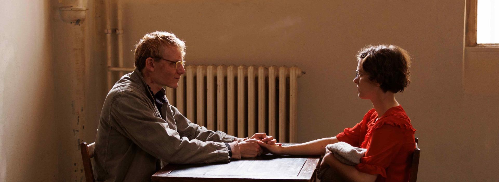 Un hombre y una mujer están sentados uno frente al otro alrededor de una mesa y se dan la mano.