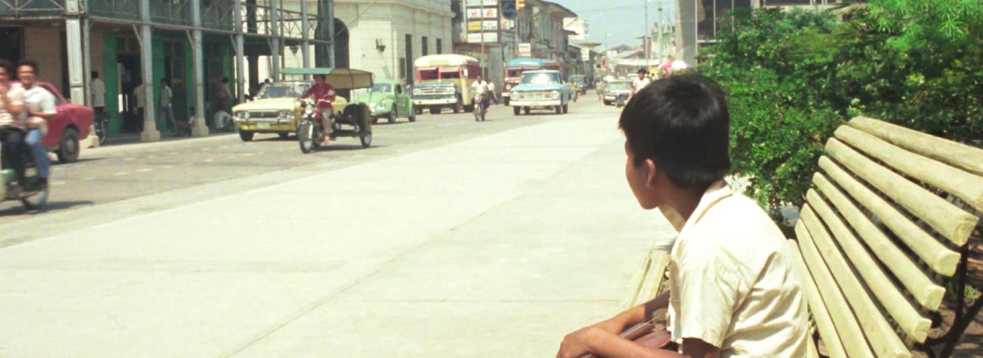Un niño mira la calle sentado en un banco.