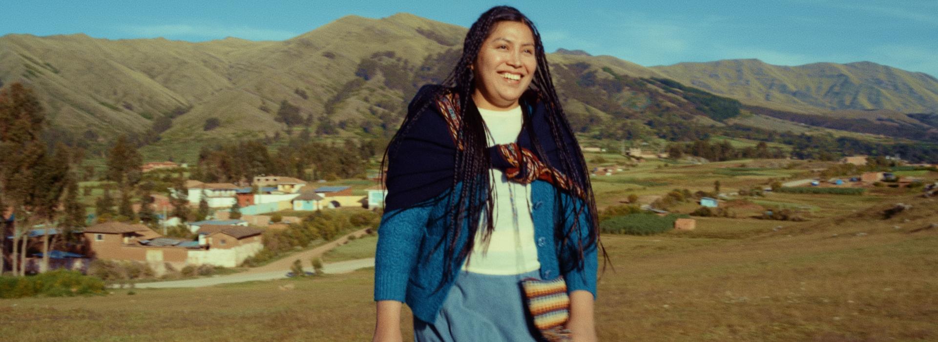 Una mujer camina y sonríe en un paisaje montañoso. 