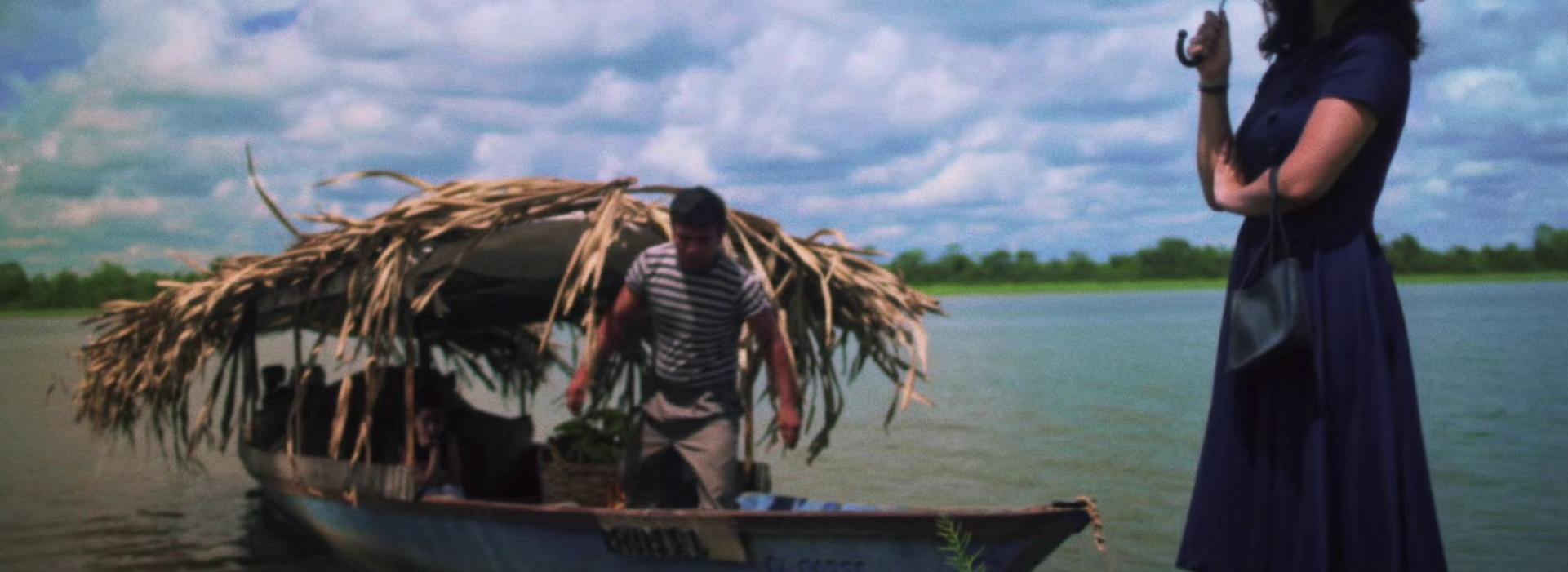 En un río, un barco y en la orilla una mujer con una sombrilla.