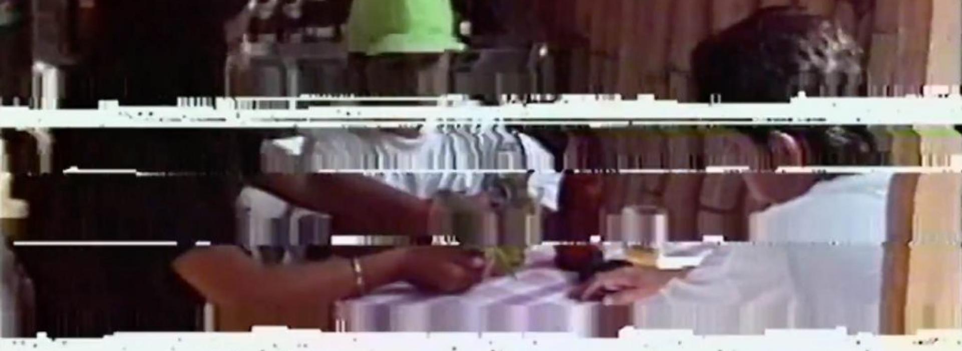 Tres personas alrededor de una mesa, pero la imagen está rayada.