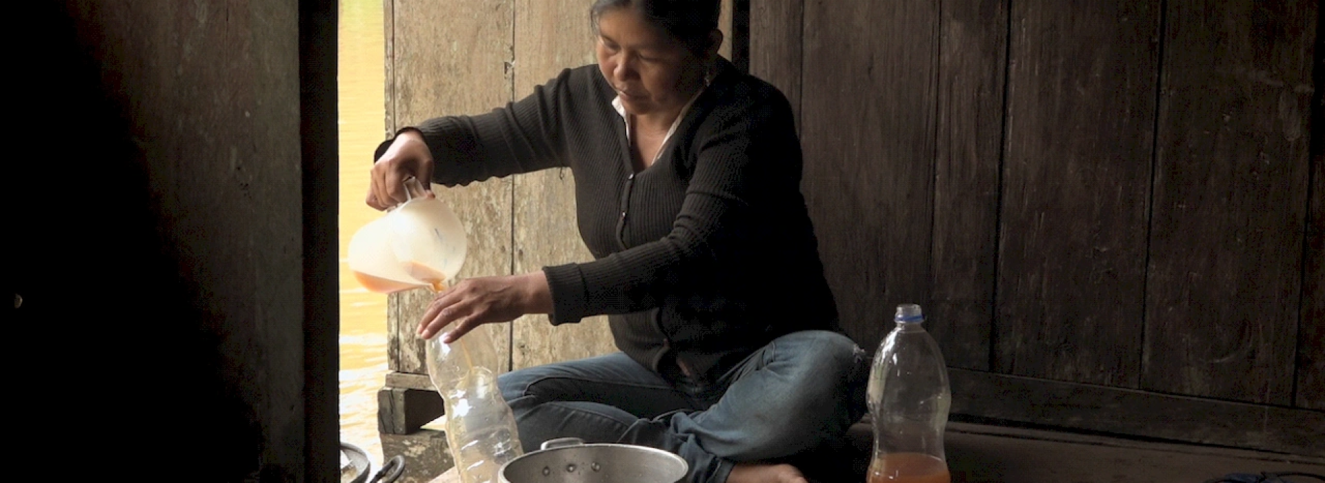 Una mujer sentada vierte un líquido en una botella.