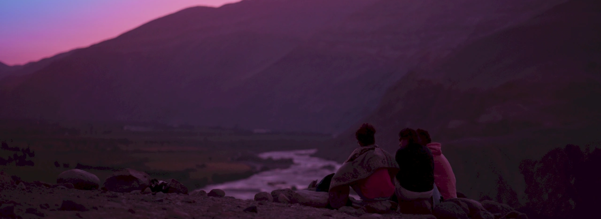 Tres jóvenes están sentados mirando un paisaje montañoso.