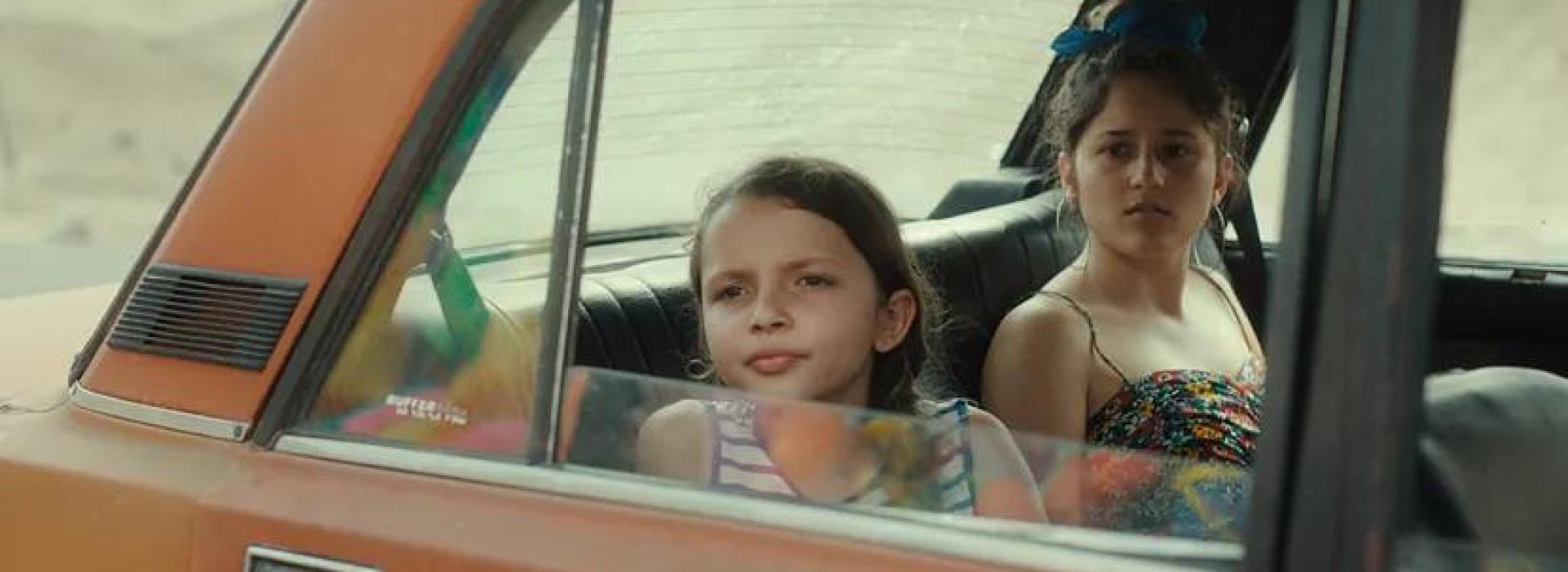 Dos chicas miran por la ventana de un coche naranja.