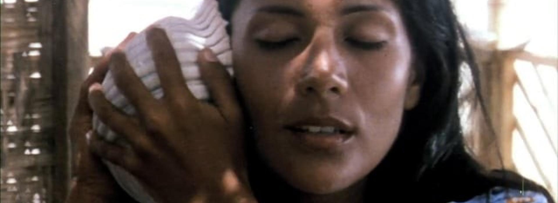 Una mujer cierra los ojos mientras escucha una concha marina.